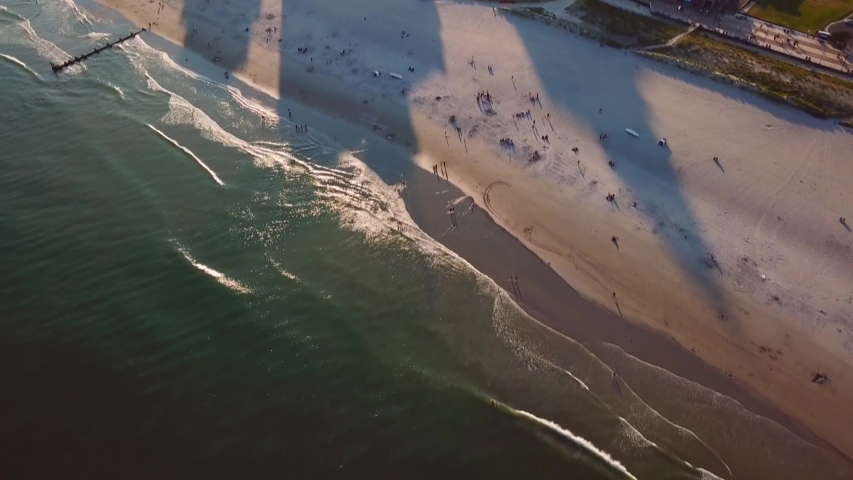 Aerial, tilt up, drone shot, over the sea and people on Chicken bone beach, revealing the high hotels, in the Atlantic city, on a sunny evening, in New Jersey, USA