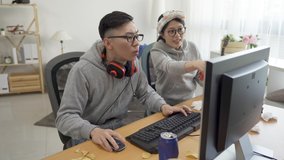 annoyed asian girlfriend sitting beside teaching talking intense telling boyfriend playing computer game. 