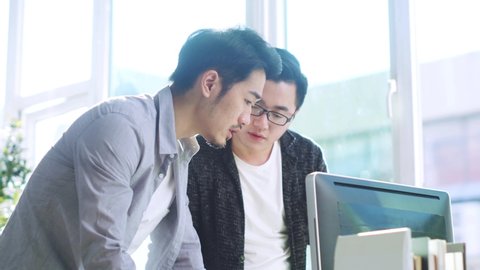 two young asian businessmen discussing business in office using desktop computer