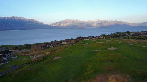 Drone Shot flying over a beautiful golf course towards Utah lake. The Wasatch mountains are in the background catching the last few rays of sunlight of the day.