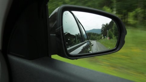 View of side mirror, reflection of a mountain road through the countryside on a summer day