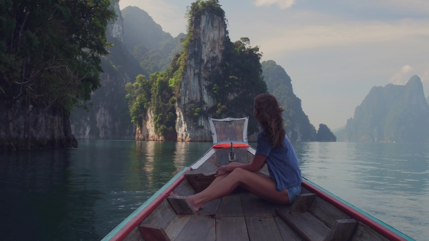 Lifestyle video of pretty travel woman sitting in wood long tail boat on tropical limestone cliffs . Explore and vacation concept. Khao Sok lake, Thailand.