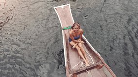 AERIAL. Lifestyle video of pretty travel woman sitting in wood long tail boat on tropical limestone cliffs . Explore and vacation concept. Khao Sok lake, Thailand.