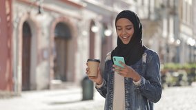 Young muslim woman wearing hijab headscarf walking in the city center, using smartphone and drinking coffee. Communication, online shopping, social network concept. - Powered by Shutterstock - Get 15% off with code: PIKWIZARD15