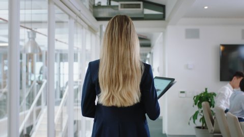 rear view blonde business woman walking through office holding tablet computer enjoying successful leadership career in corporate workplace 4k