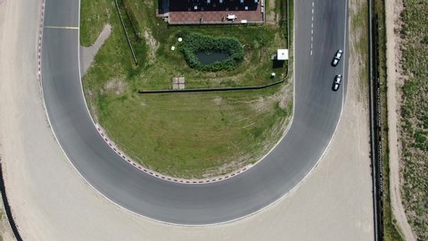 Top down 4k aerial video of cars drifting synchronized in formation on race track through 180 degree turn creating tire tracks on the asphalt