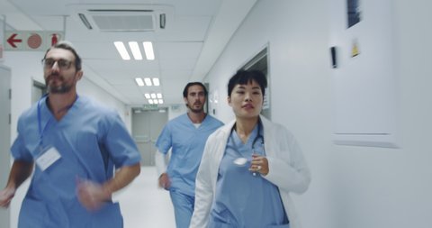 Reverse tracking shot of young Asian female doctor and male interns running through hospital corridor responding to an emergency. Healthcare workers in the Coronavirus Covid19 pandemic