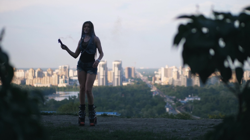 The girl dances in angoo jumps shoes in the background of the city. She has a blue smoke checker in her hands.
