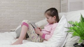 sad little child girl lies in bed uses digital tablet. something is wrong