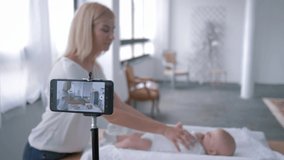 videoblog, young mother uses a mobile phone and does exercises for her little daughter lying on the changing table