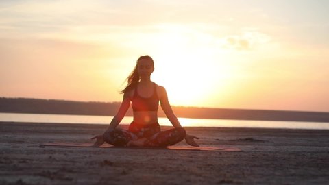 slim woman practices yoga poses improving mental physical health on sea beach against pictorial orange sunset backside