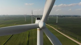 Drone flying away from an up close shot of a wind turbine nose cone to show a field of wind generators.