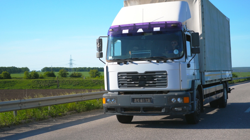 Camera follows to truck with cargo trailer driving on highway and transporting goods at summer day. Lorry riding through countryside with nature landscape at background. Slow mo Front view Close up | Shutterstock HD Video #1033282061