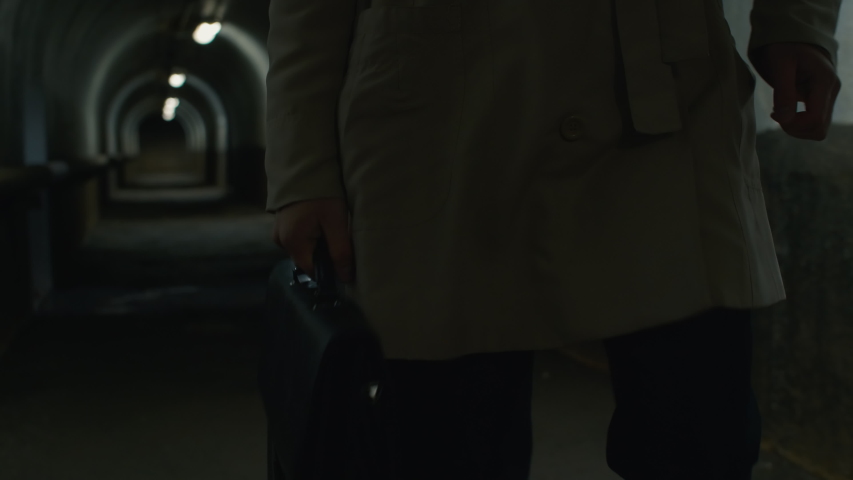 Tilt up shot of businessman going through the tunnel with case and helmet under his arm, taking helmet and putting it on head