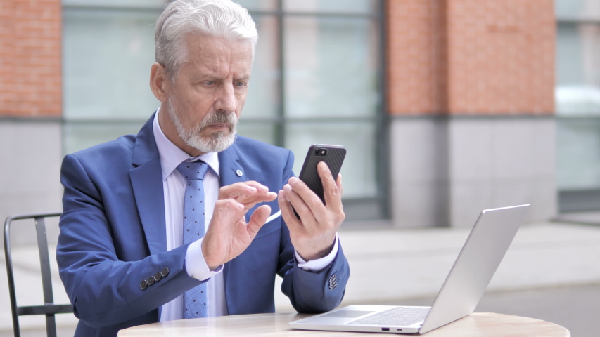 Old Businessman Upset by Loss while Using Smartphone