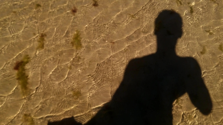 Silhouette shadow of a man on a sandy beach with waves, pov shot