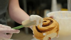 woman puts icing glaze on large cinnamon role in slow motion. Woman ices large cinnamon role in this slow motion clip.