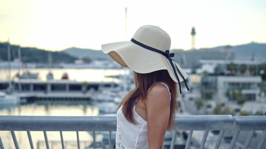 Pretty woman wearing white dress and pamela hat walking over the beach terrace at sea. Happy summer vacation