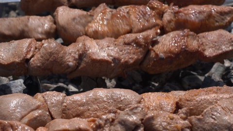 Appetizing juicy pork shish kebabs cooking on metal skewers on charcoal grill with fragrant fire smoke. Cooking during summer picnic. Close-up view, selective focus on tasty pieces of roast meat.