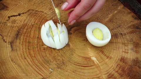 A woman is cutting eggs. Female hands close-up. The concept of recreation, eating and cooking in nature. Cutting of products on a wooden board, as ingredients for salad on open air.