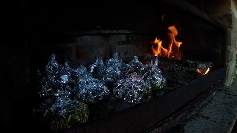 A foil wrapped dish placed on a hot coals in a fireplace of red bricks. Slow motion