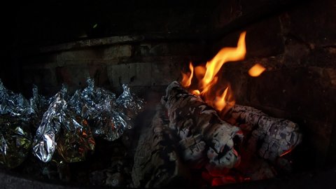 A foil wrapped dish placed on a hot coals in a fireplace of red bricks. Slow motion