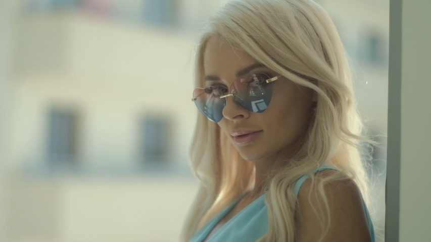 Beautiful smiling blonde woman with sunglasses, close up indoors room at home or hotel.   Bright lady with good mood.  
