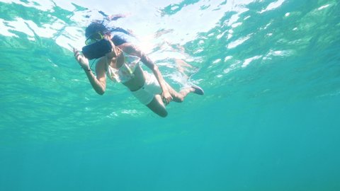 Snorkling woman taking photo to underwater world in transparent sea water. Young woman swimming in snorkeling mask and tube and shooting video to mobile in protective cover.
