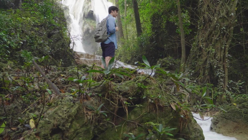 Young Man Standing In Front Of A Waterfall
