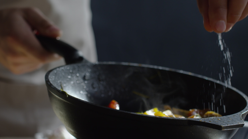 Close up of chef hand holding hot pan and adding salt to it with other hand Royalty-Free Stock Footage #1033365887