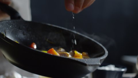 Close up of chef hand holding hot pan and adding salt to it with other hand