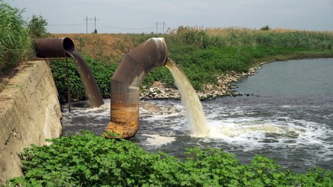 Wastewater from two large rusty pipes merge into the river in clouds of steam