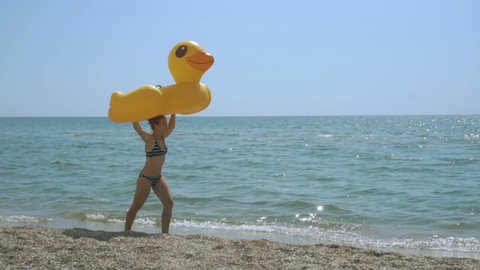 Woman walking on empty beach holding inflatable duck