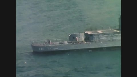 CIRCA 1967 - Guns fire from an aircraft carrier towards the shore, during the Vietnam War.