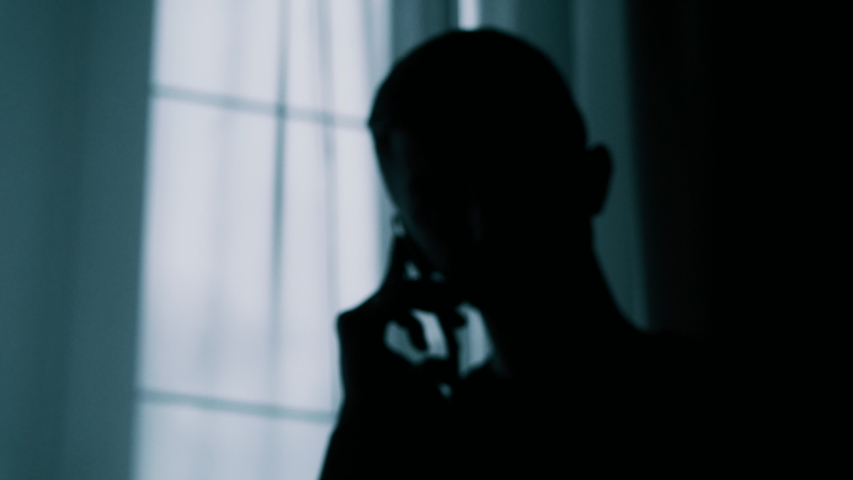 Anonymous blurred silhouette of a man talking on a cell phone in a dark room, a criminal is extorting money Royalty-Free Stock Footage #1033386554