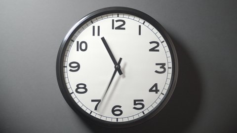 Closeup of White Clock Face in timelapse in daytime of office dark grey wall
