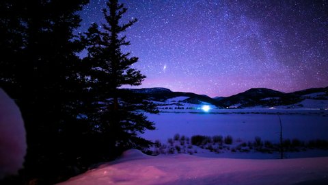 Starlapse of Blue and Purples on the Snow with Silhouetted Trees to Look Up Intro the Blurry Sky