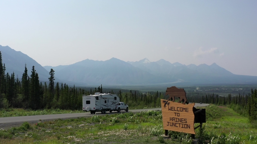 Welcome to Haines Junction sign with people driving towards Haines Junction and the Kluane Mountains.