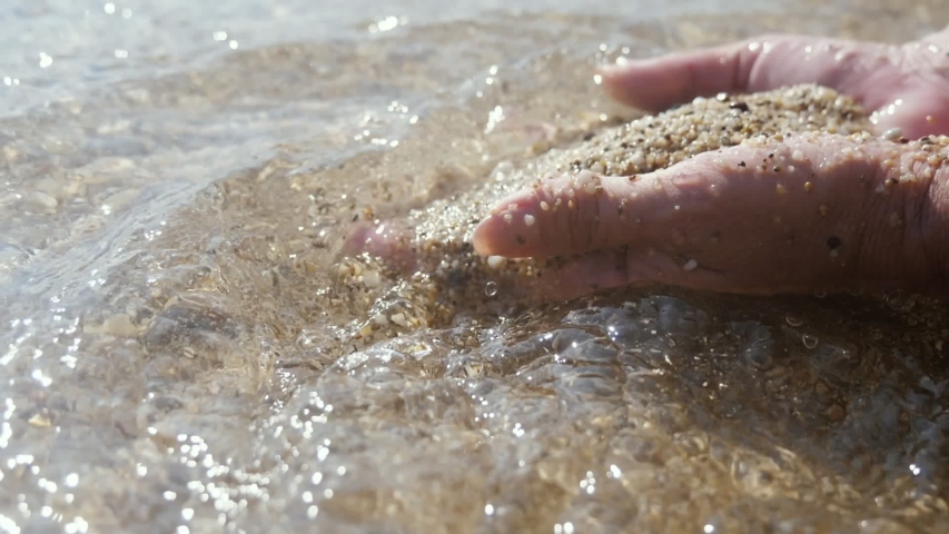 Wonderful view of two male hands digging and playing wet sand and shells on...
