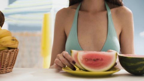 Cute happy young woman sitting at the beach bar and eating a fresh delicious watermelon, summer and healthy food concept