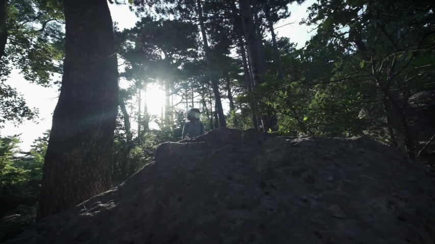 SLOW MOTION, CLOSE UP: Unrecognizable courageous male hiker climbing mountaintop, walking off trail on dangerous rocky mountain ridge. Steep wall opening beautiful view on the forest.