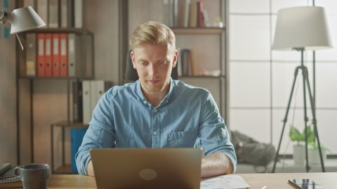 Handsome Young Entrepreneur Works in Office Closes His Laptop Computer, Picks Up Smartphone from the Desk and Leaves Work