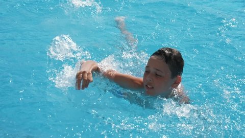  Cheerful view of an energetic ten-years-old boy swimming freestyle in a paddling pond with sparkling aqua waters in slo-mo
