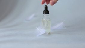 woman's hand holding a pipette from a glass bottle cosmetic essence. Drop falling from a pipette on a blue background with white feathers Video Slow motion