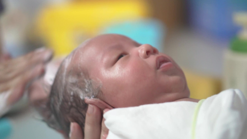 Close up of father and mother wash newborn baby boy hairs in the bathtub