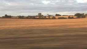 Wide shot out of a window of aing train, tracking along flat british countryside and farmland