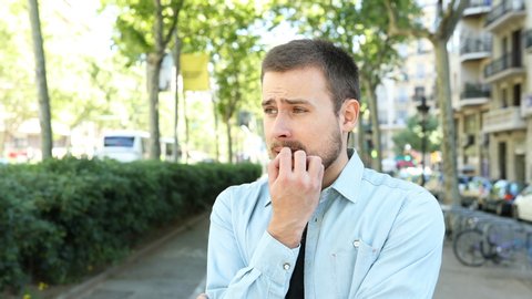 Nervous man biting nails looking away standing in the street bedore first date