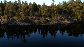 Aerial video flying towards lake rocky shore and up above rocks and pine trees revealing breathtaking northern landscape with lakes and endless boreal pine trees coniferous forest going over horizon.