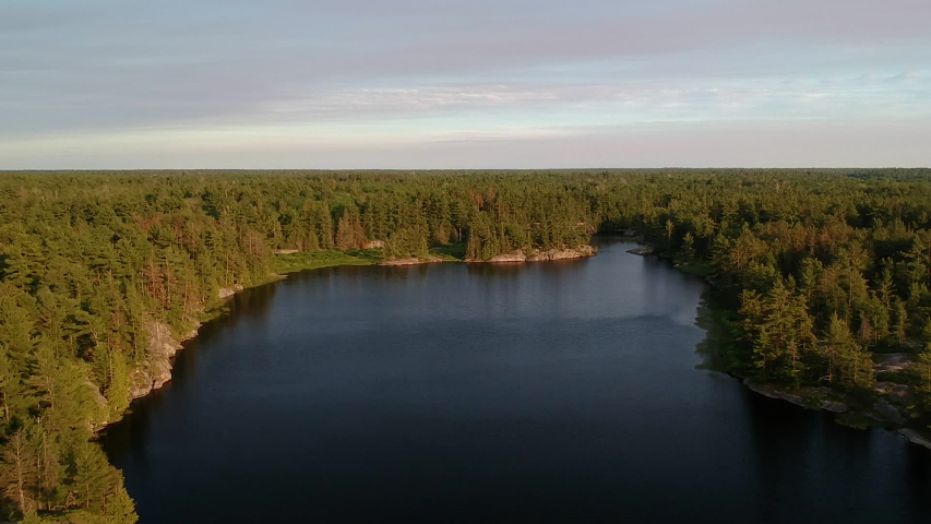 Aerial shot of norhtern lake revealing endless boreal coniferous pine forest going over horizon at sunset. Camera moves straight up. Pedestal shot. Grundy Lake, Northern Ontario, Canada