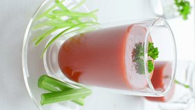 a glass of organic tomato juice with parsley and celery on white table, vertical video